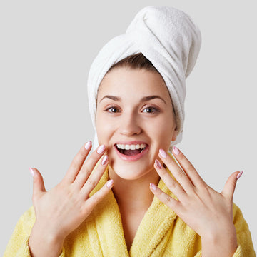 Woman in yellow robe with towel on head showing her nails against a light gray background